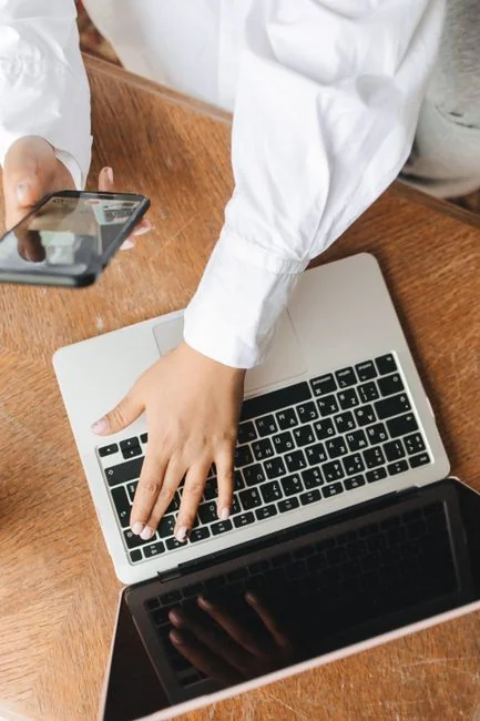 Two business professionals review stock market data on a smartphone and laptop in a contemporary office environment.